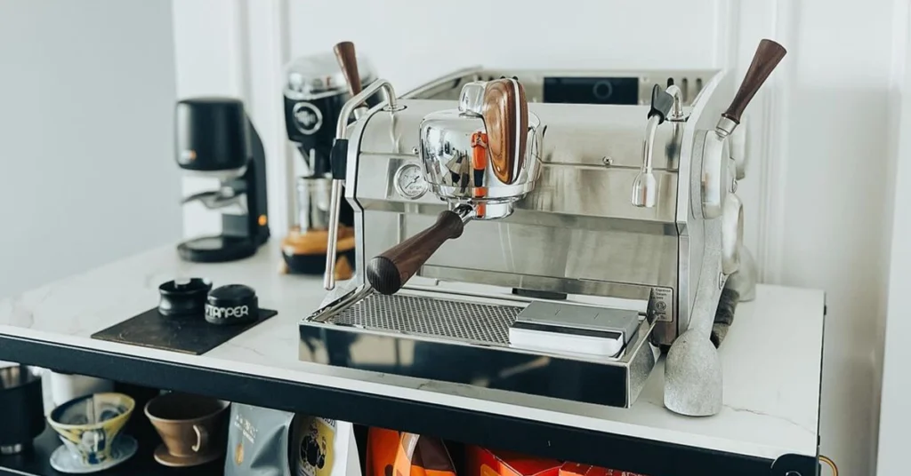 A modern espresso machine with wooden accents sits on a kitchen counter, flanked by a coffee grinder and cups.