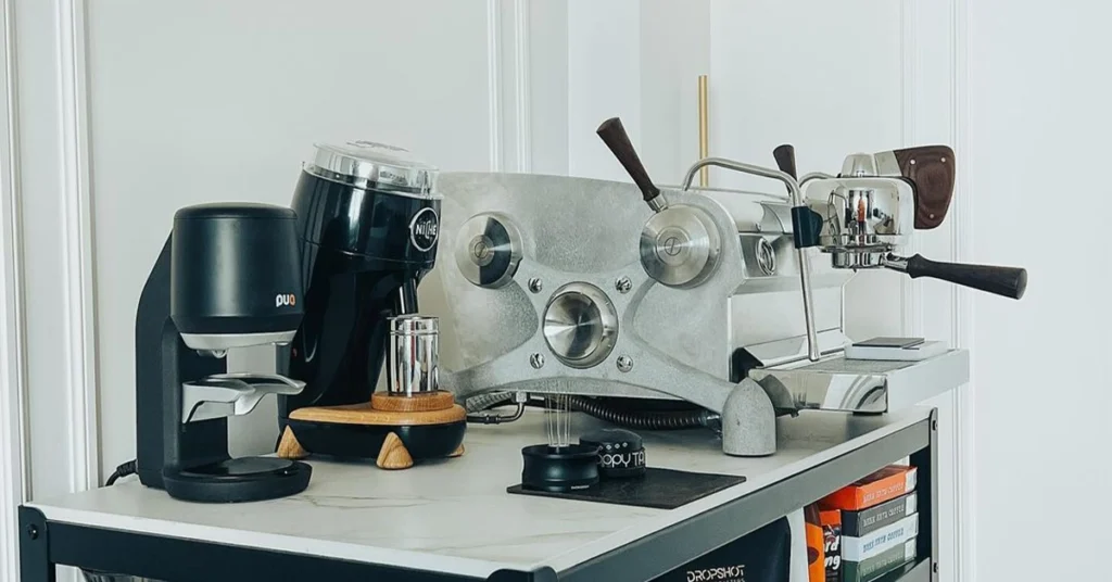 A sleek coffee setup with an espresso machine, grinder, and accessories on a countertop, with shelves holding coffee beans below.